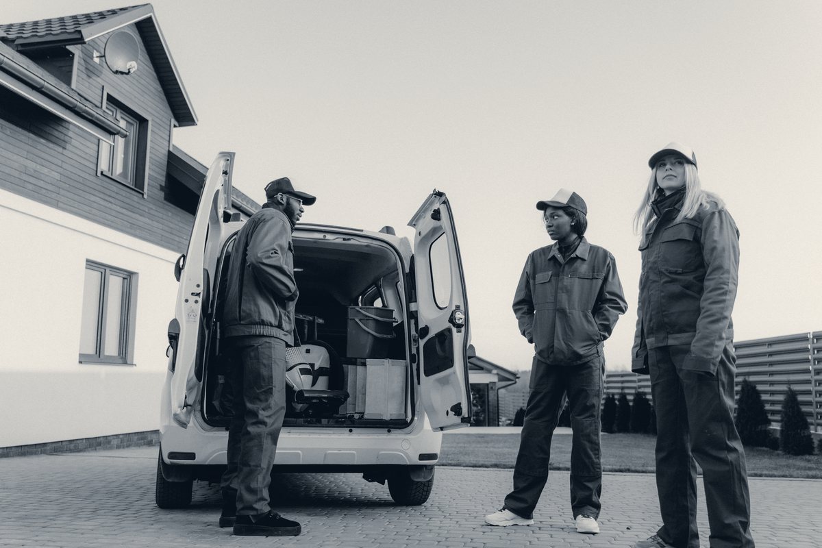 An HVAC owner and two of his technicians in uniform at the back of a loaded service van outside a customer's home.